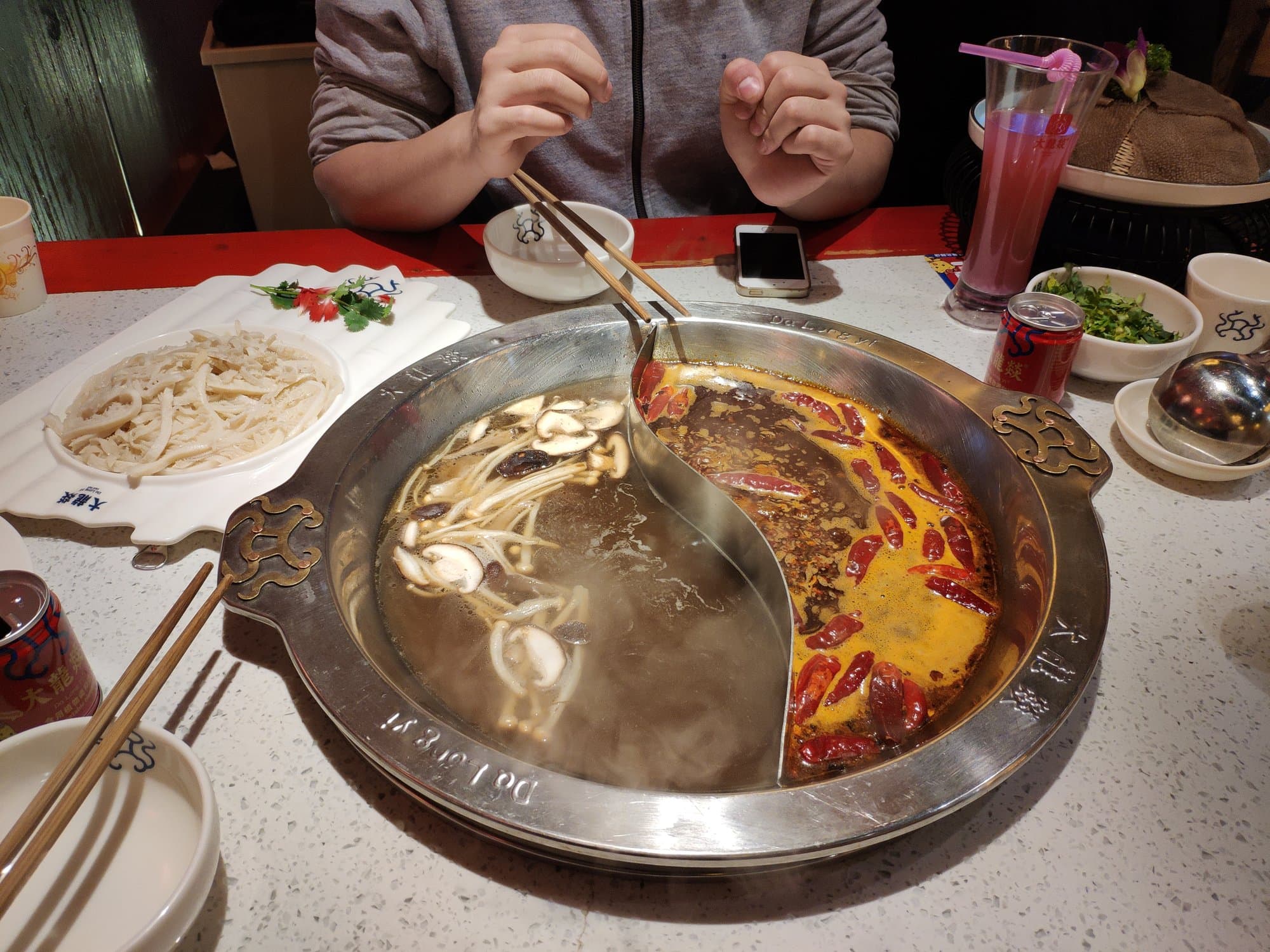 A divided hot pot in a Chengdu restaurant, red chile broth on one side and a pale broth with enoki mushrooms on the other