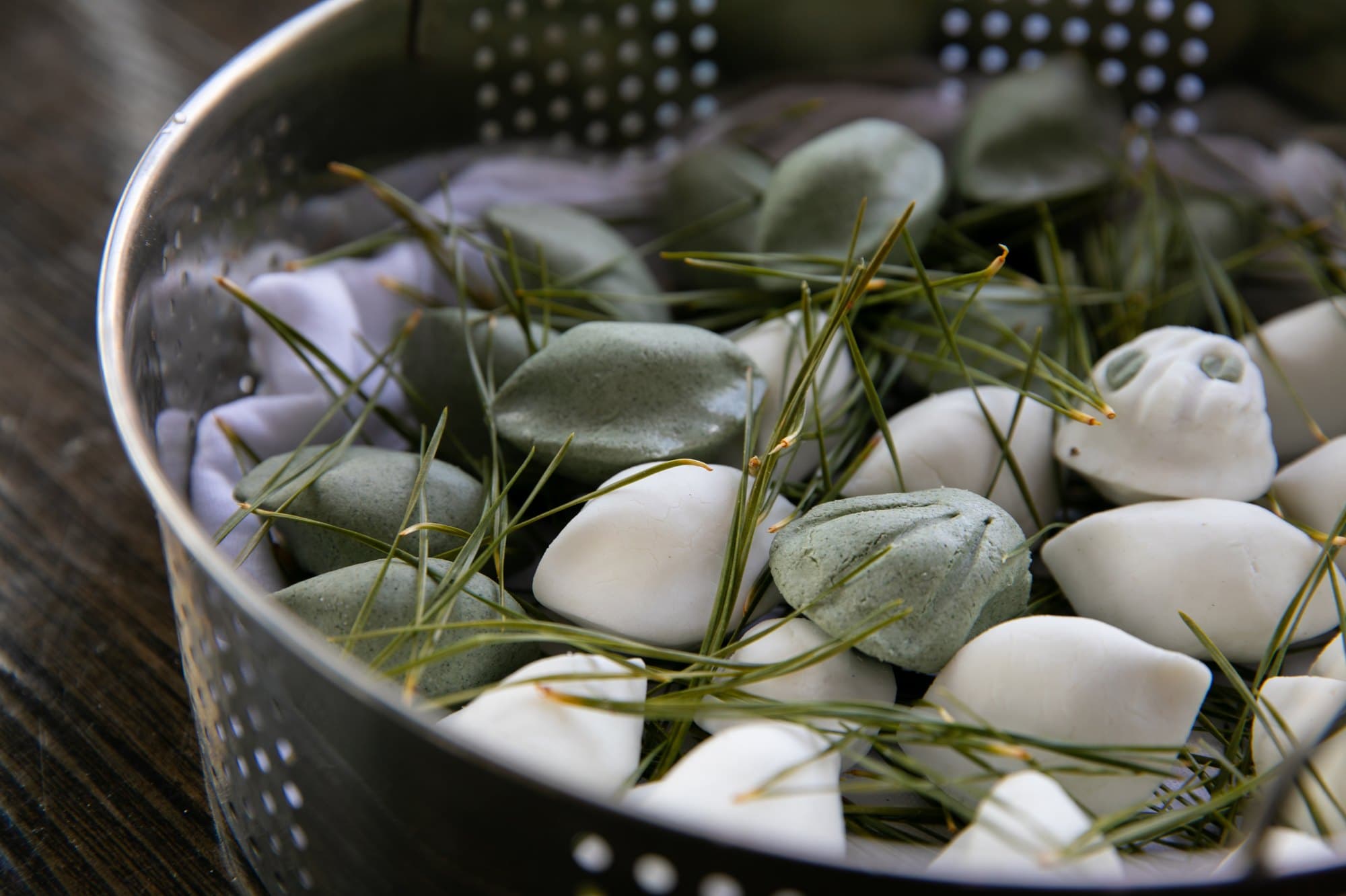 White and mugwort-green songpyeon with pine needles in a metal steamer