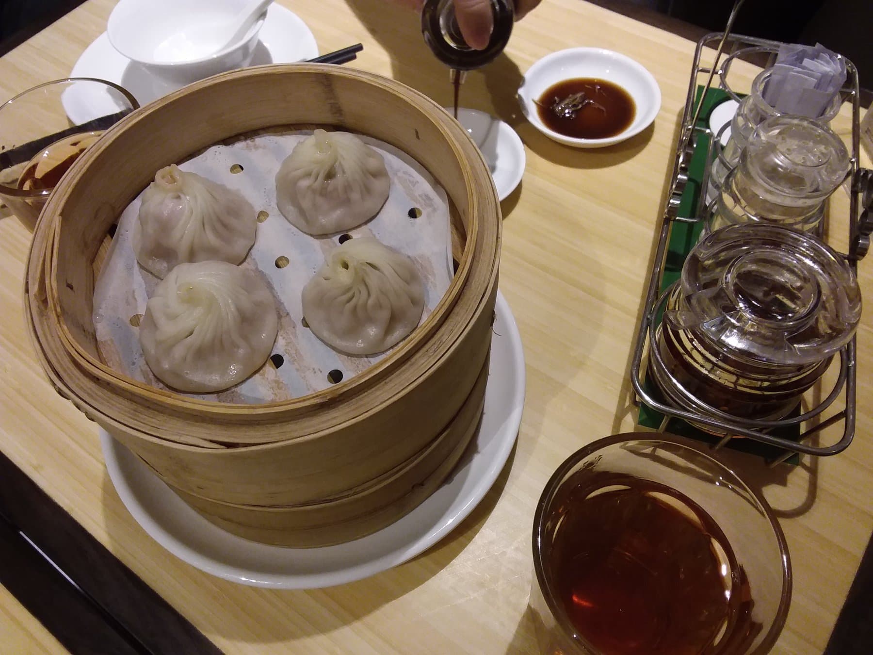 Bamboo steamer of Crystal Jade xiao long bao with vinegar and ginger on a wood table