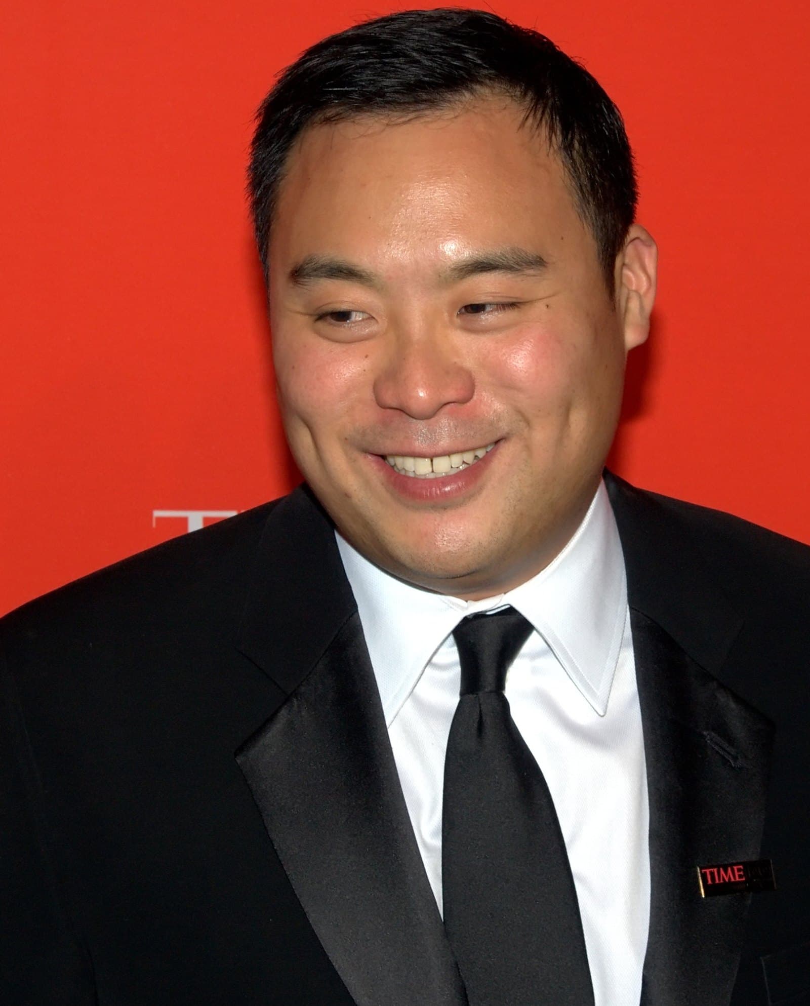 Portrait of David Chang in a tuxedo against a red backdrop