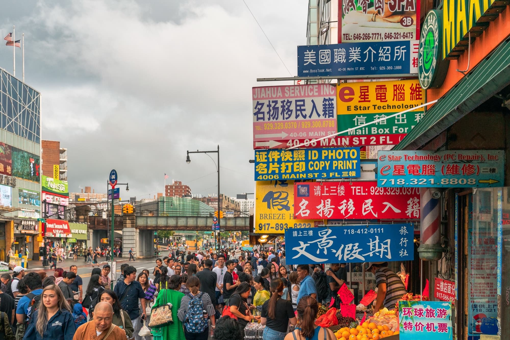 Crowded Main Street sidewalk in Flushing with layered Chinese and English storefront signs