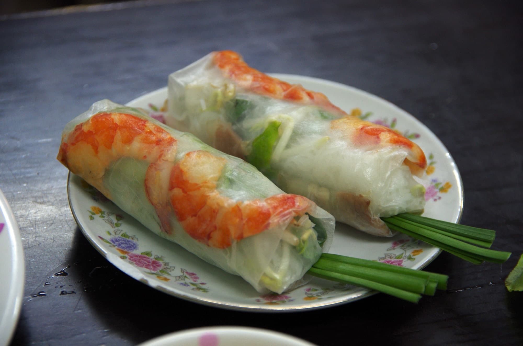 Two Vietnamese shrimp summer rolls with garlic chives on a small floral plate