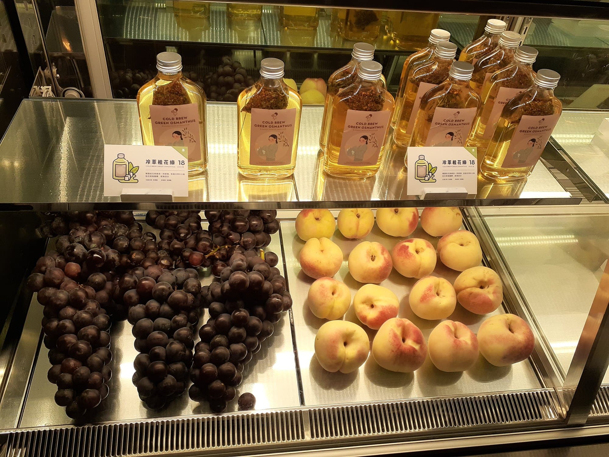 Heytea cold-brew osmanthus bottles above grapes and peaches in a glass case