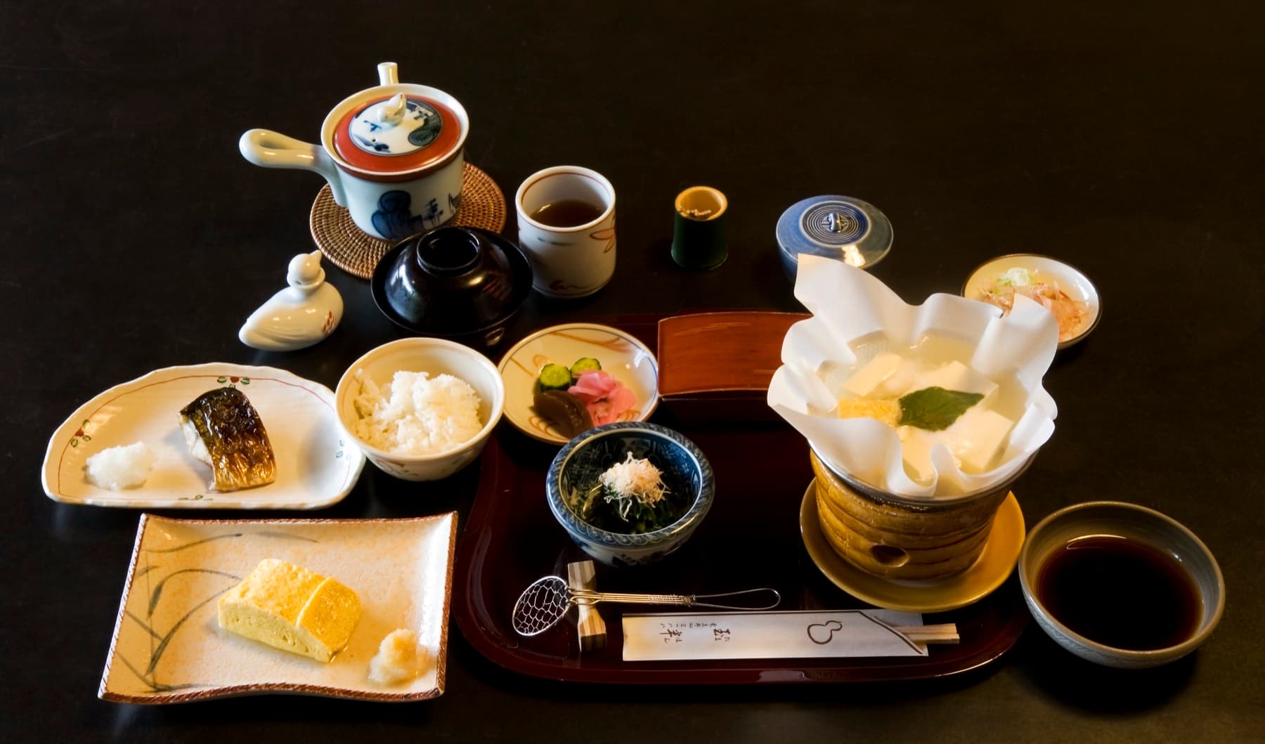 Overhead Japanese breakfast tray with grilled fish, rice, miso soup, tamagoyaki, tofu, and pickles