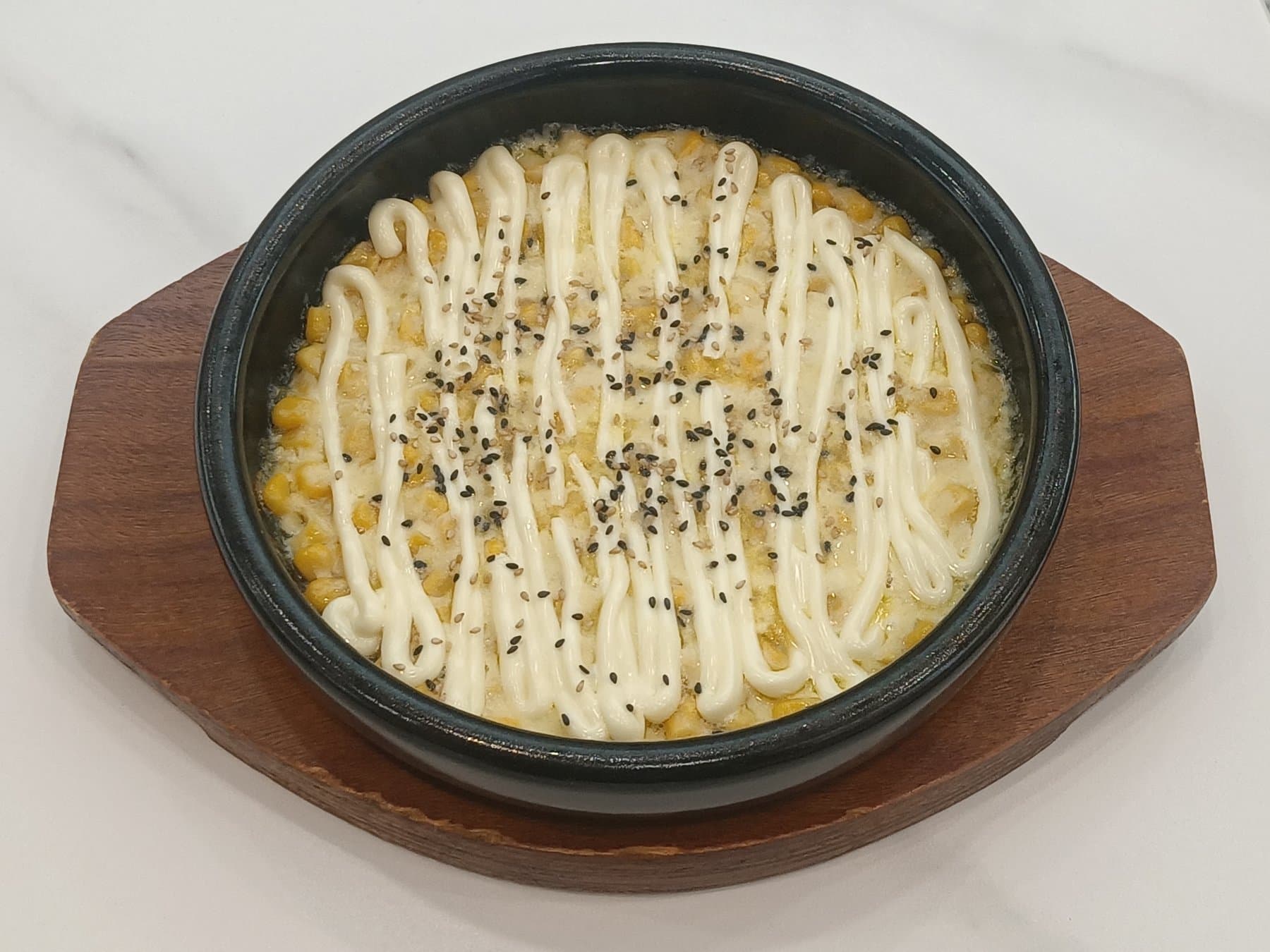 Korean corn cheese in a black skillet with mayo drizzle and sesame seeds