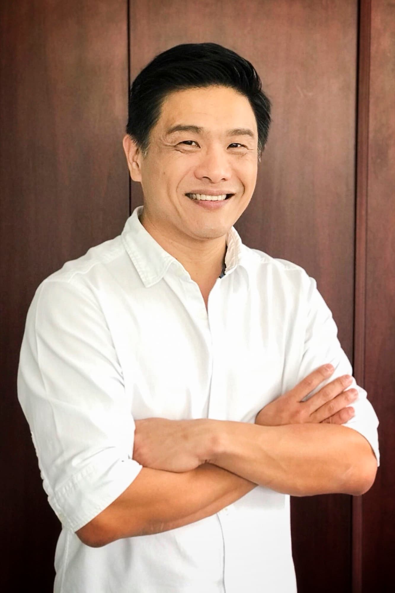 Portrait of Dr Leslie Tay in a white shirt, arms crossed, smiling