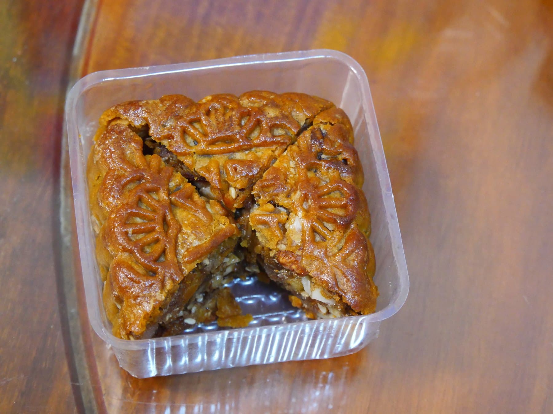 Cut five-nut mooncake in a clear plastic tray on a wood table, filling visible