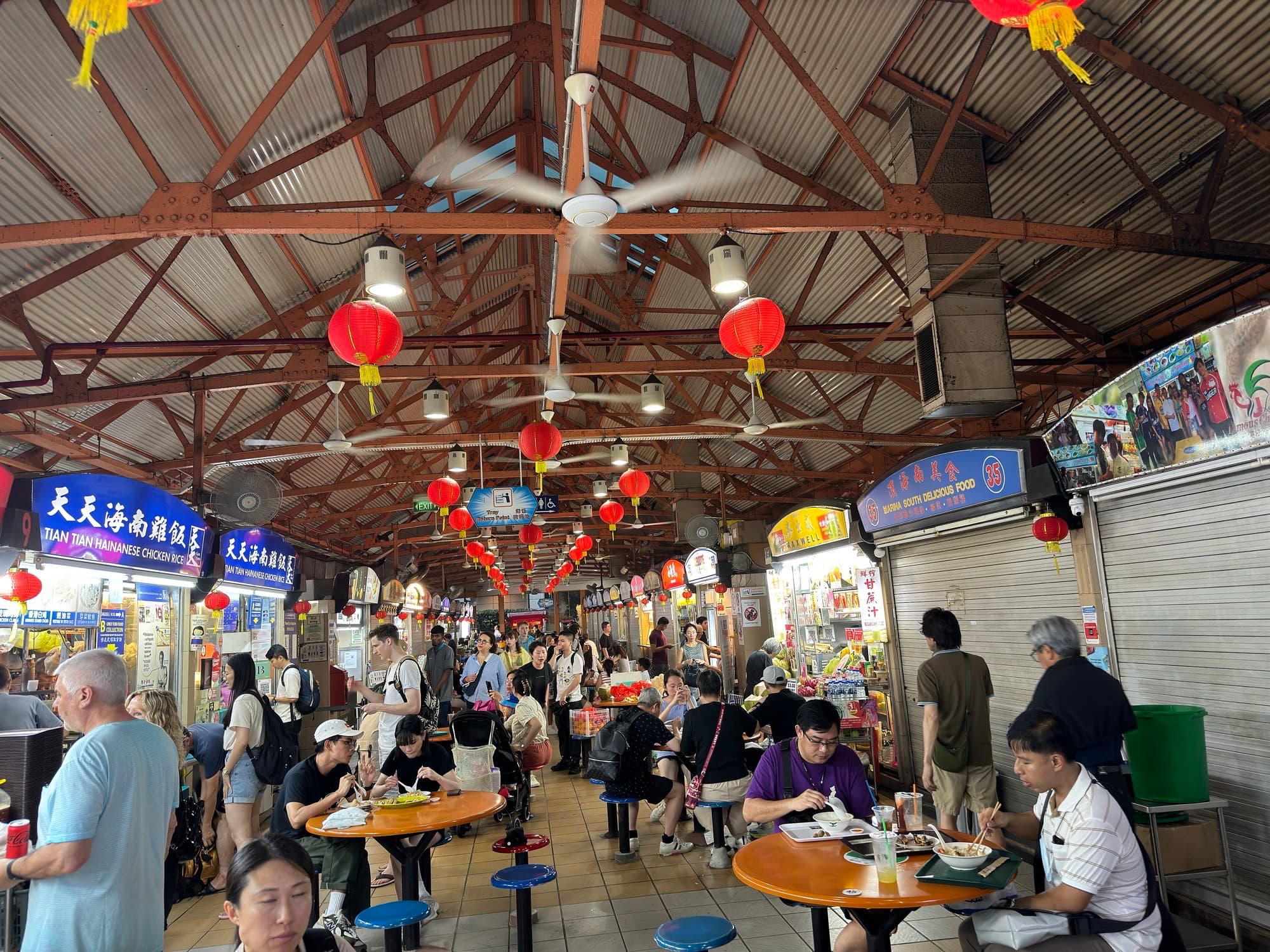 Busy Maxwell Food Centre interior with red lanterns, communal tables, and chicken rice stall signs