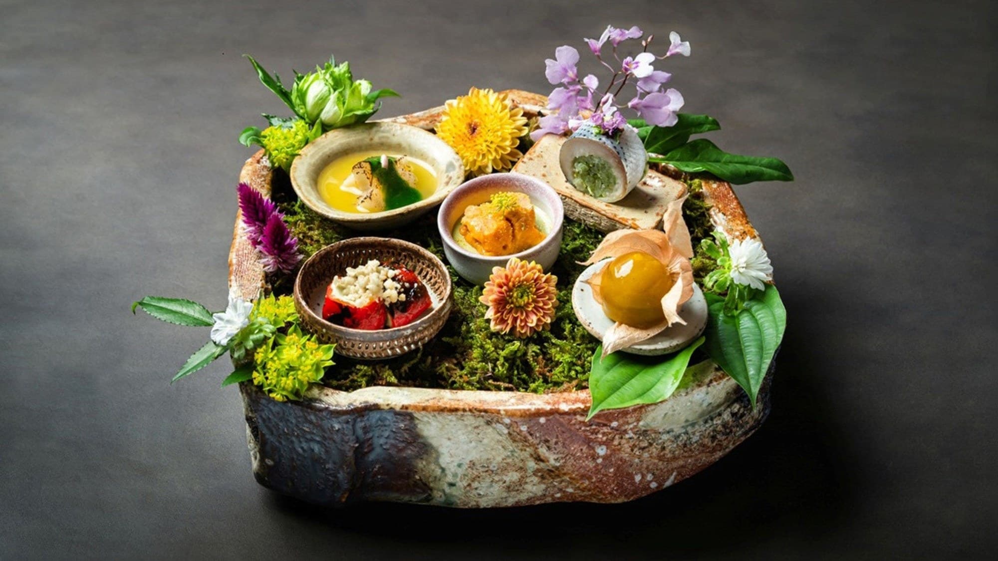 A composed course on moss in a rustic ceramic vessel, with small bowls, edible flowers, and a physalis, at SoNoMa by SingleThread in Kyoto