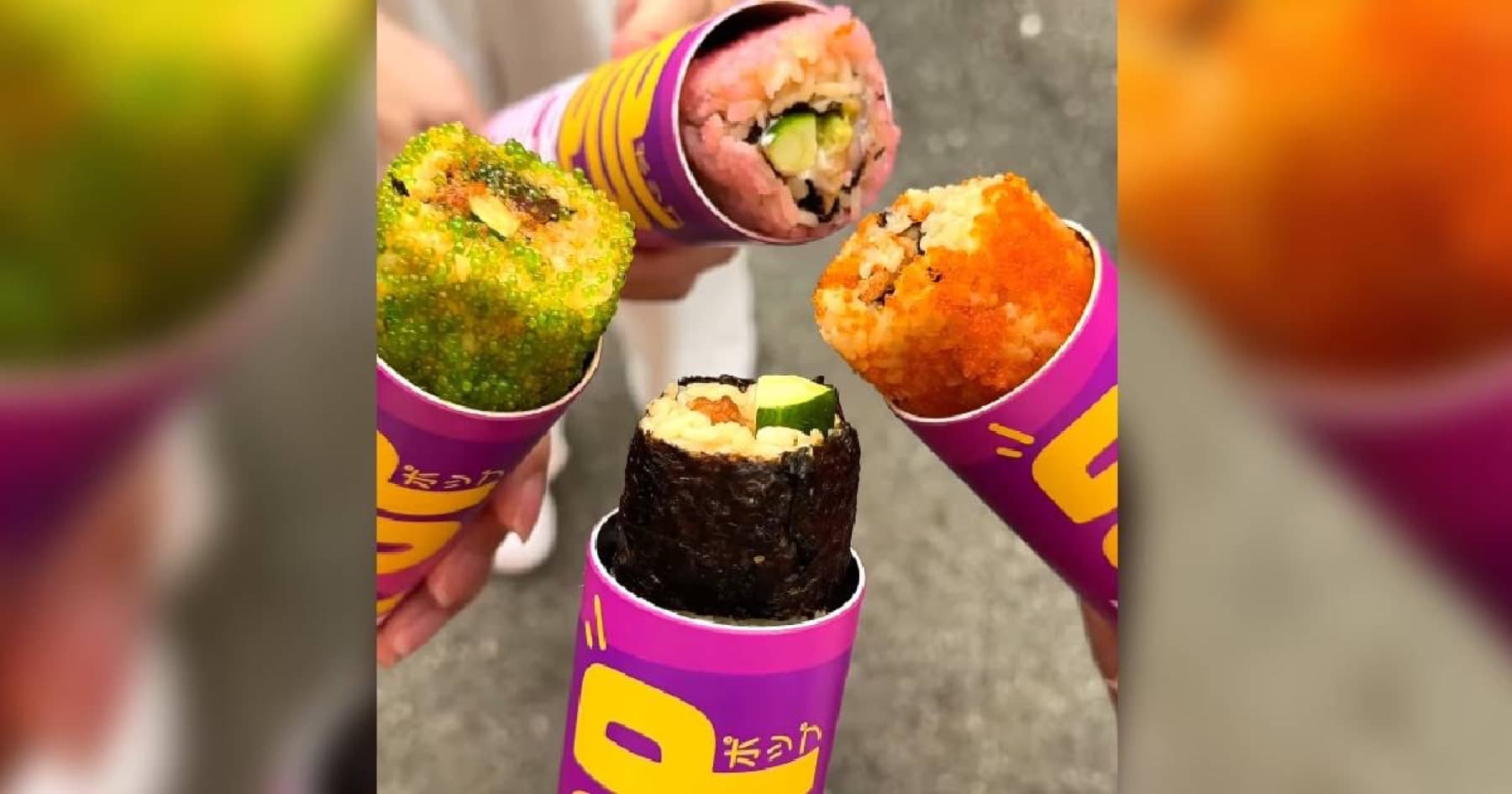 Four hands holding purple SushiPOP tubes with colorful maki pushed out the tops