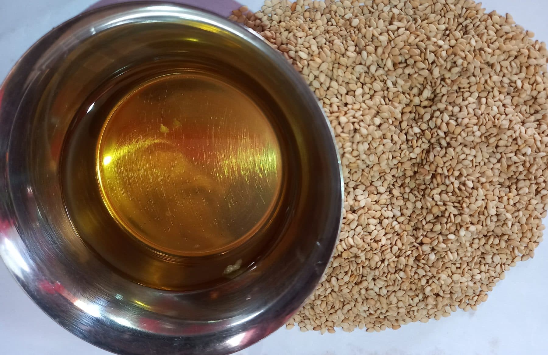 Small metal bowl of amber toasted sesame oil beside a pile of toasted sesame seeds