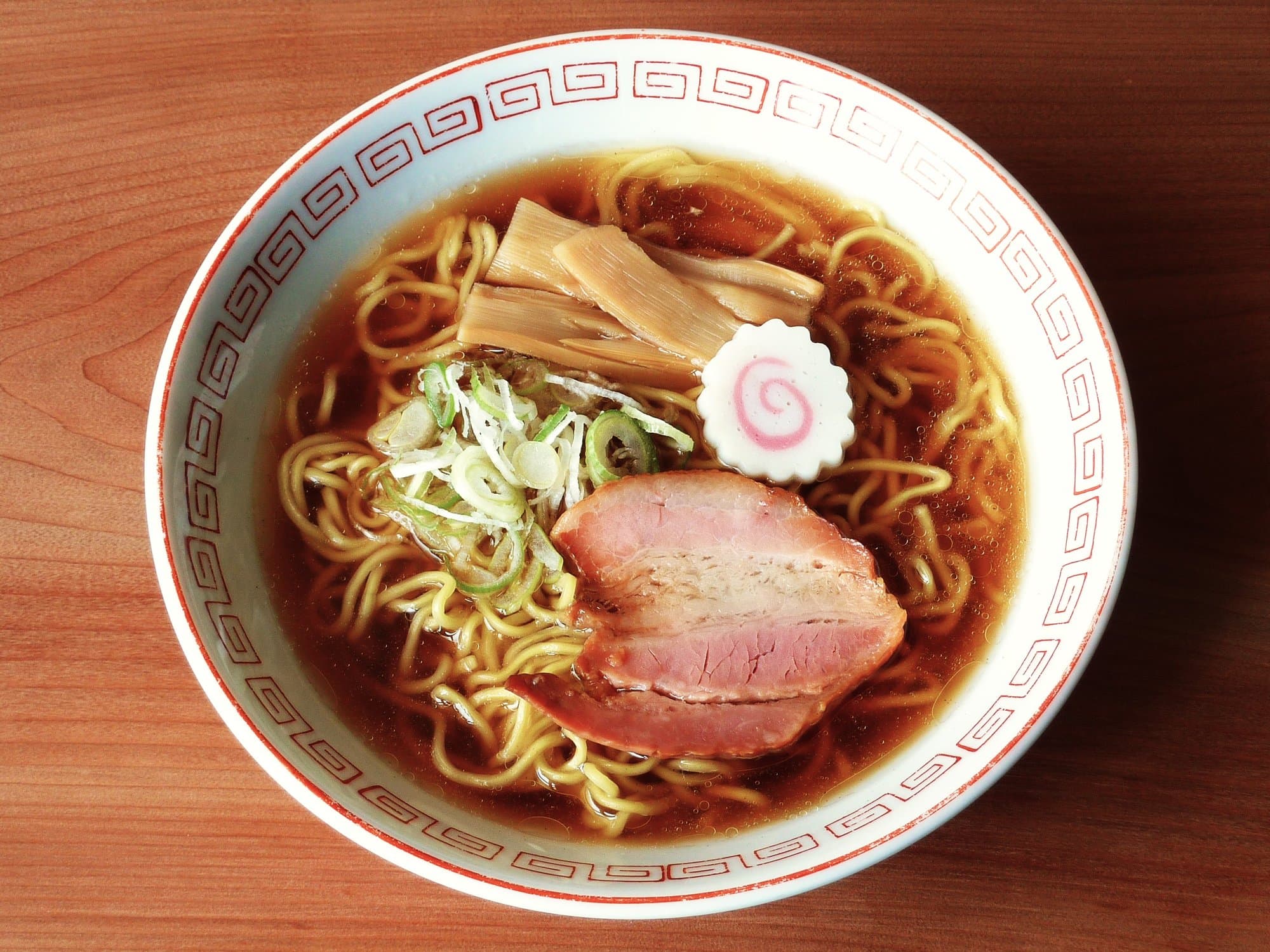 A bowl of Tokyo-style shoyu ramen with wavy noodles, chashu, menma, scallions, and a slice of naruto fish cake