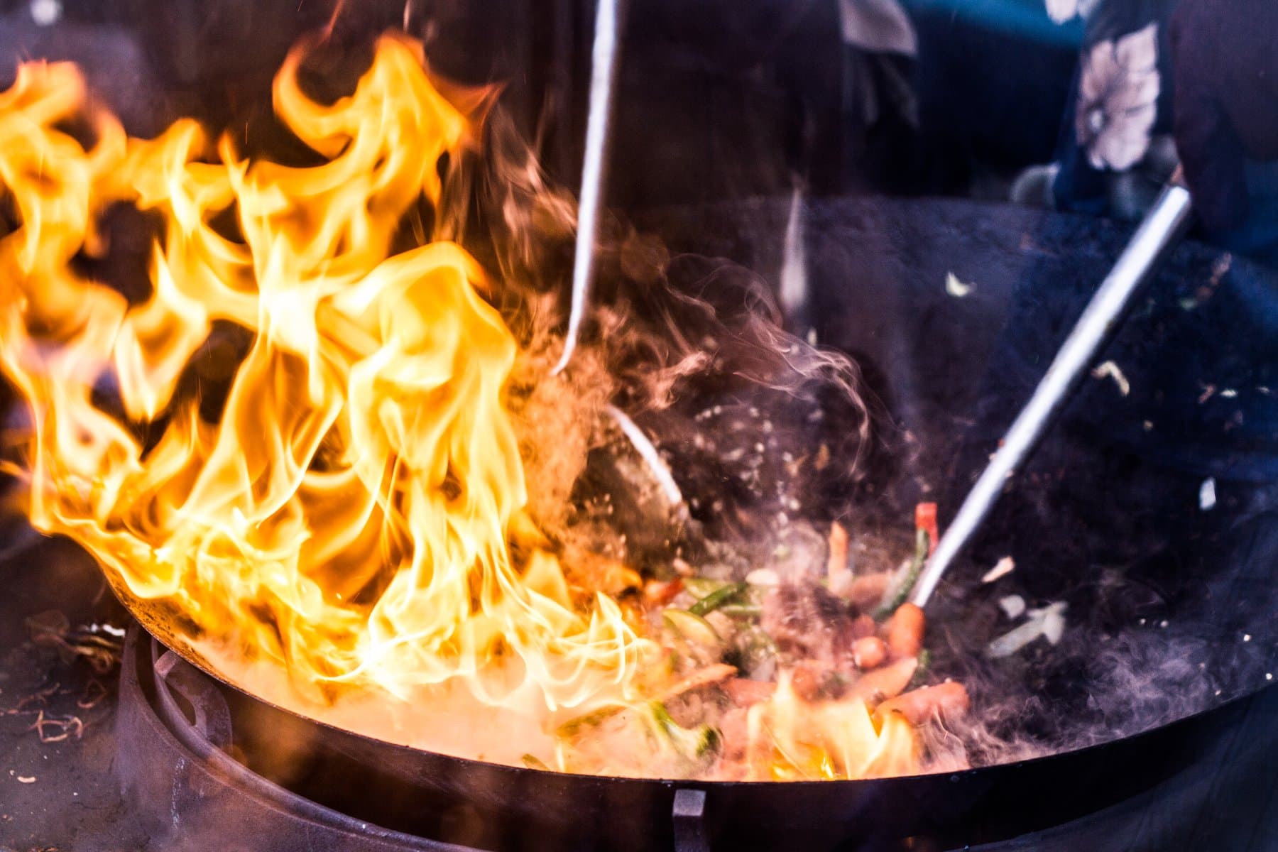 Flames rising from a wok as vegetables are tossed over high heat